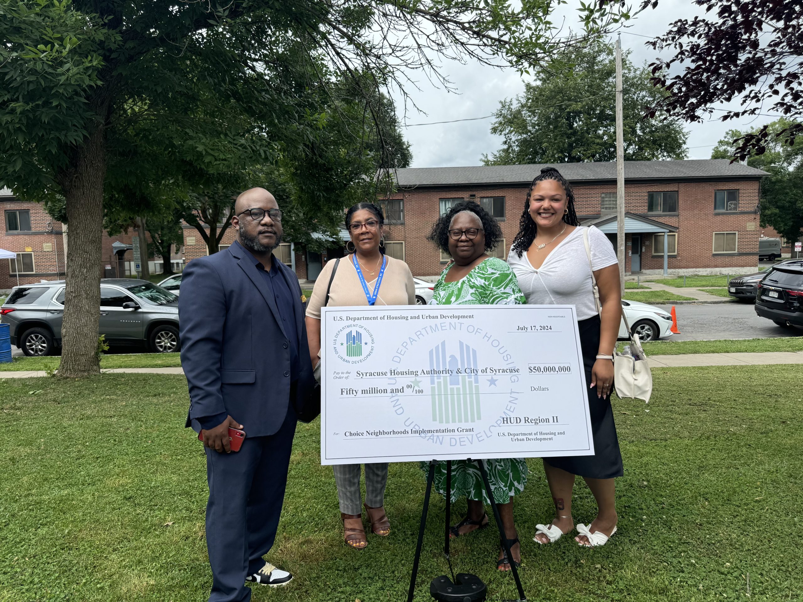 USI Staff stand around a giant check from the US Department of Housing and Urban Development (HUD) in the East Adams, Syracuse, NY. Community for a Choice Neighborhoods Grant. 